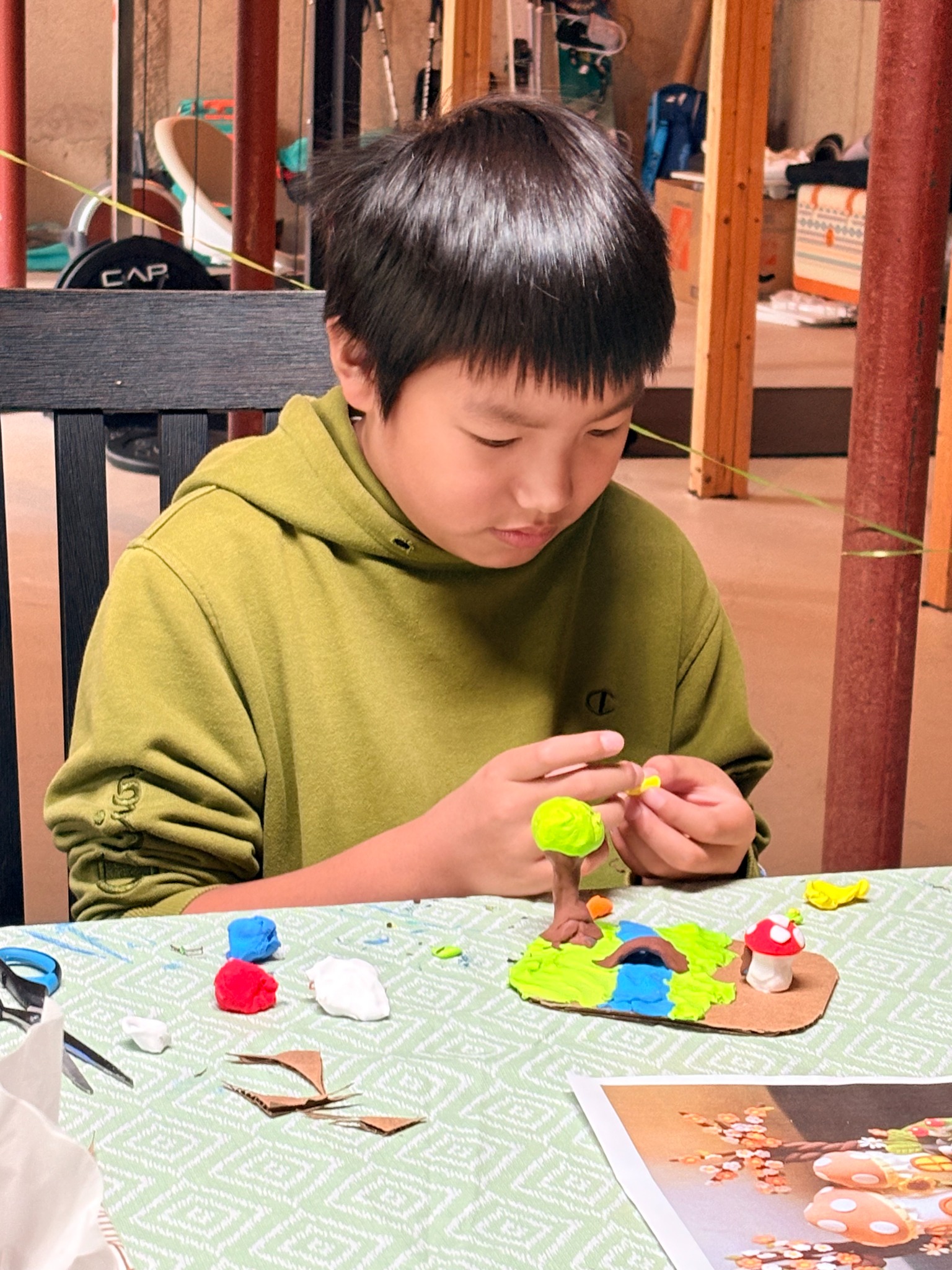 A child shaping a clay tree beside a miniature landscape